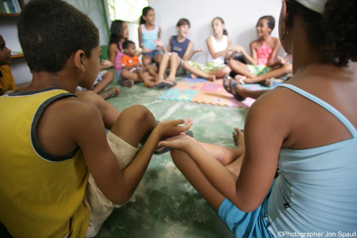 Children sit in circle holding hands at a Promundo meeting