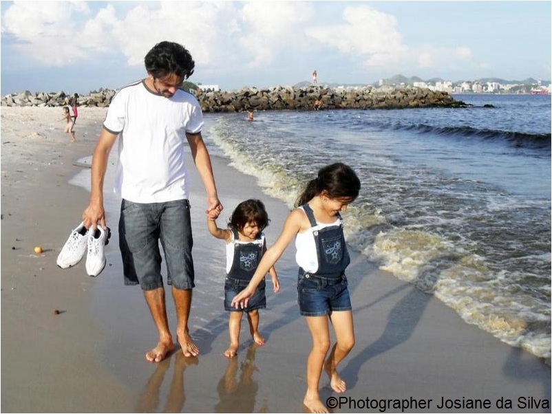 Father holds his two daughters hands as they play on the beach